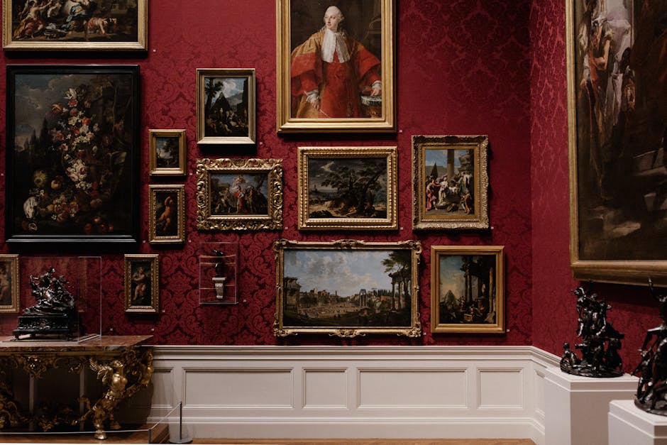 A spacious art gallery with a high, arched ceiling featuring large skylights, allowing natural light to illuminate the room. The light-colored wooden floors are clean and polished, reflecting the brig