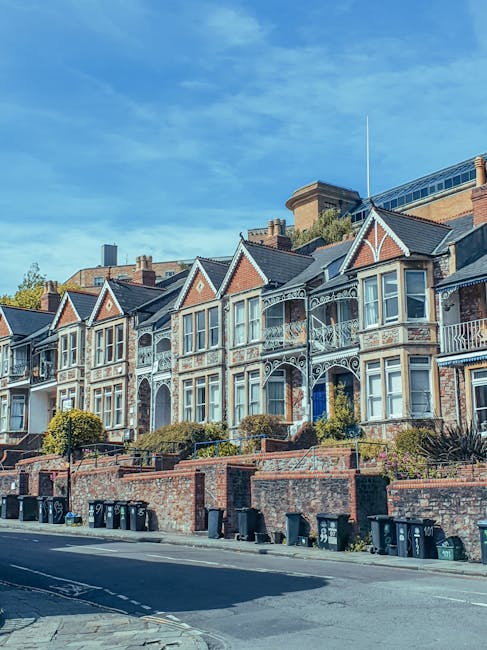 A row of traditional Victorian terraced houses with intricate white ironwork balconies and bay windows on the upper floors. The buildings are constructed with red brick and feature tiled roofs with po